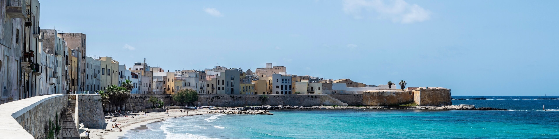 Uma vila costeira com calçadão, mar azul-turquesa e edifícios coloridos.