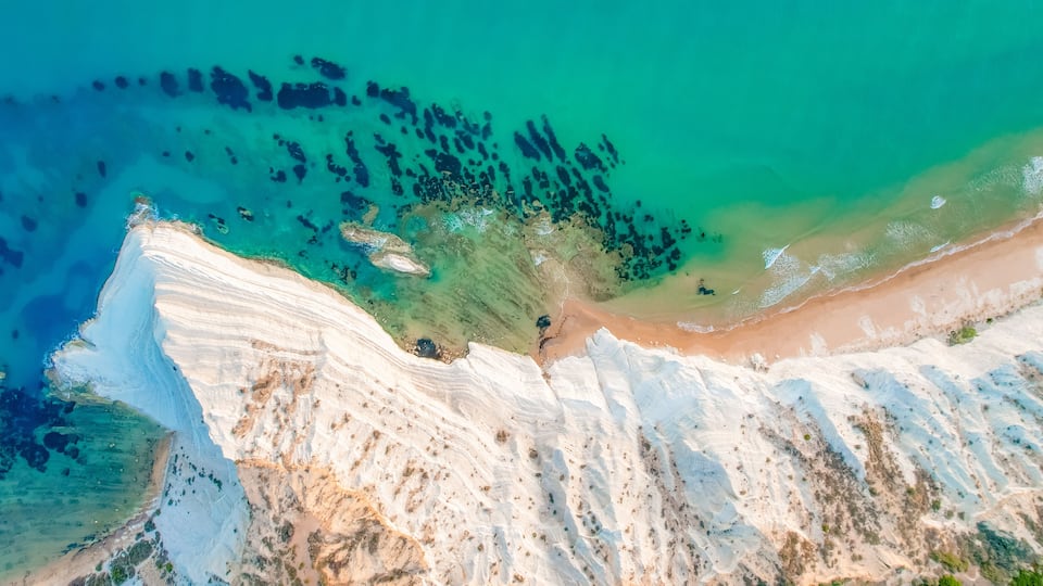 A coastal landscape with white cliffs, a sandy beach, and clear turquoise waters.