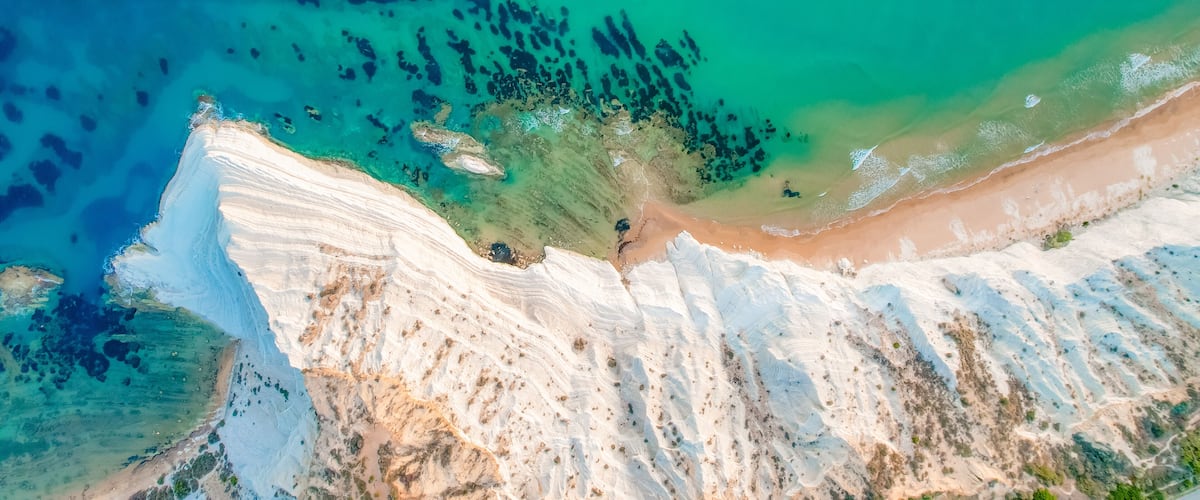 A coastal landscape with white cliffs, a sandy beach, and clear turquoise waters.