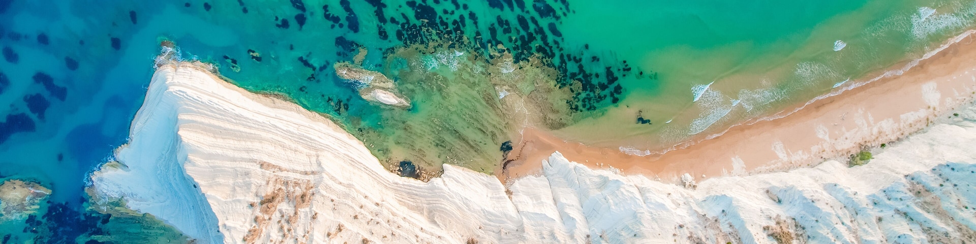 A coastal landscape with white cliffs, a sandy beach, and clear turquoise waters.