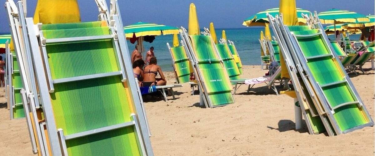 Beach chairs and umbrellas lined up on a sandy beach with a clear blue sky.