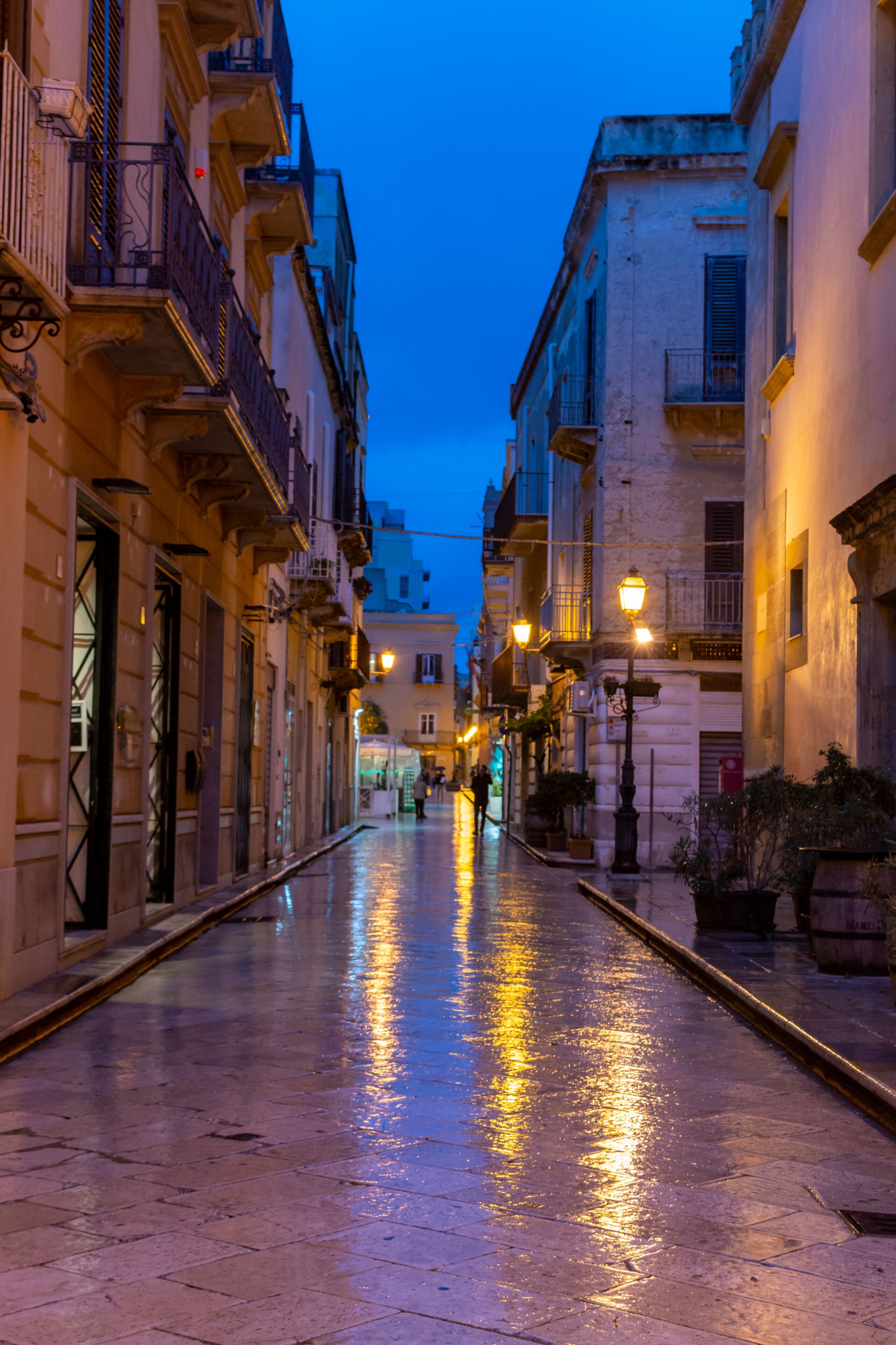 Old street in Marsala at night in rain with reflection of street lights on water, Sicily, Italy