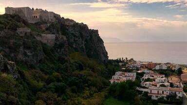 A coastal town with a historic castle on a cliff, surrounded by lush greenery and a clear view of the sea.