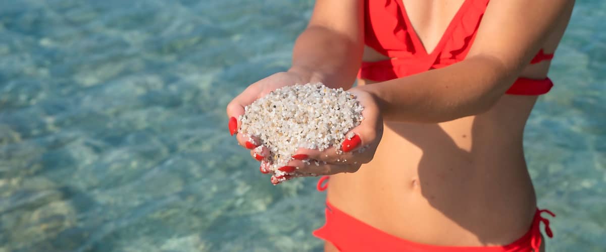 A person holding a handful of small white objects, likely seashells, on a beach.