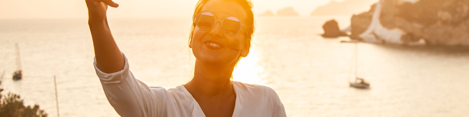 Una persona tomándose un selfie junto a la playa con un atardecer de fondo.