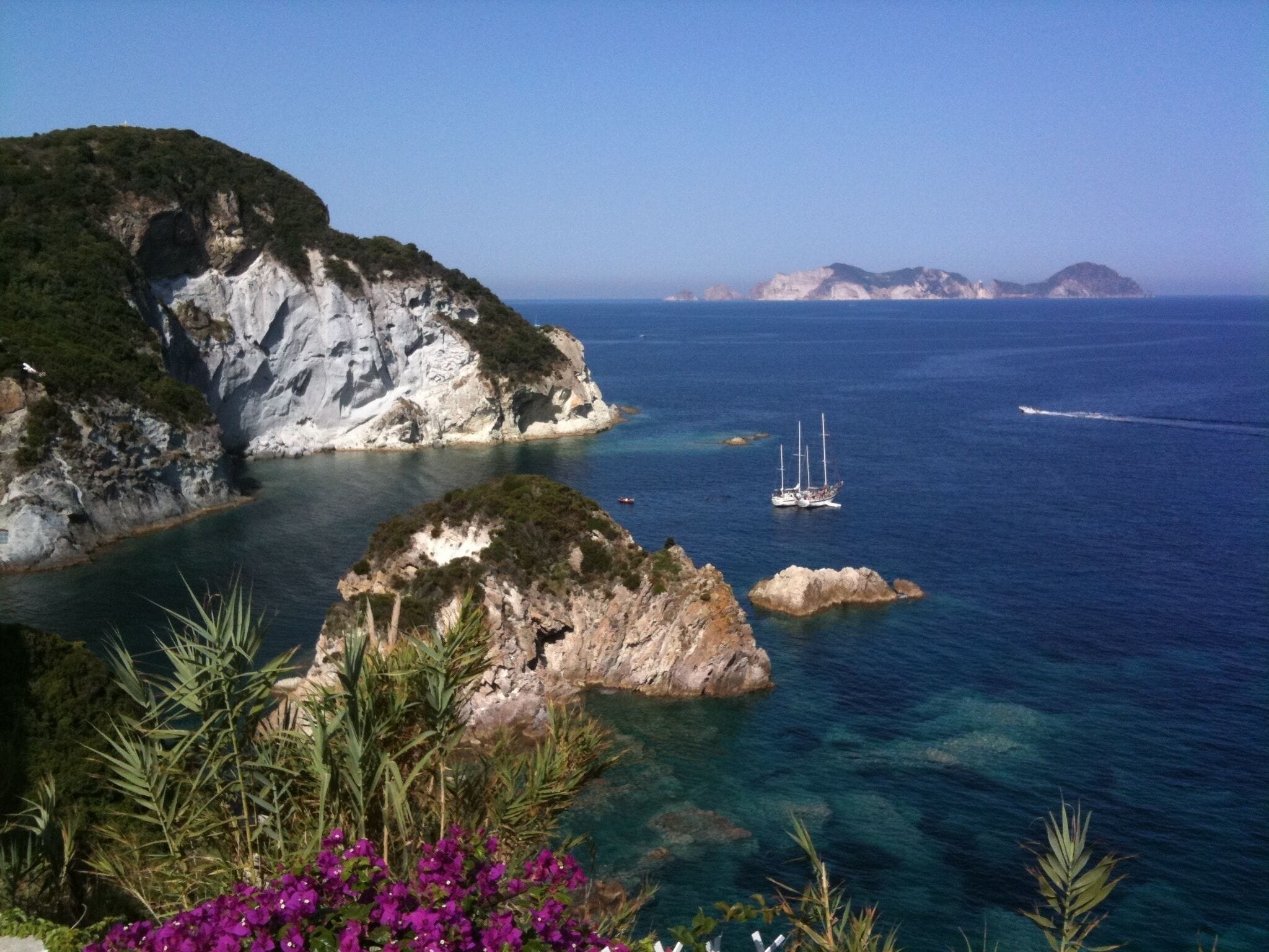A coastal landscape with rocky cliffs, clear blue sea, and a sailboat.