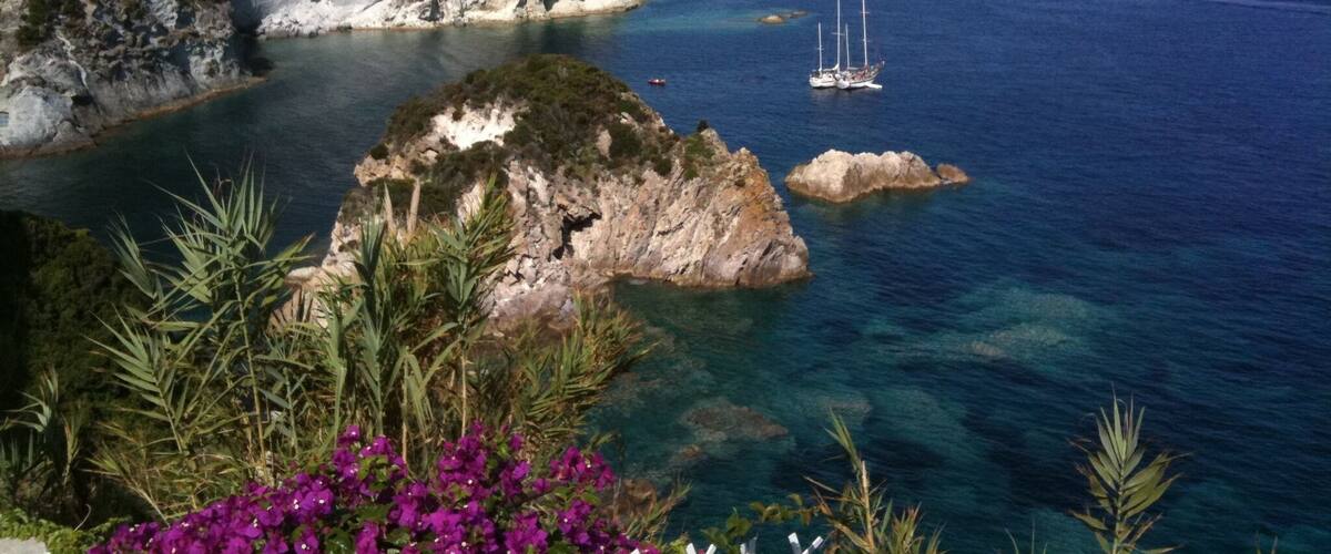 A coastal landscape with rocky cliffs, clear blue sea, and a sailboat.