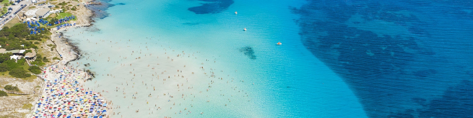 Une plage cĂŽtiĂšre aux eaux turquoise et limpides, un promontoire rocheux et une petite Ăźle surmontĂ©e dâune tour.