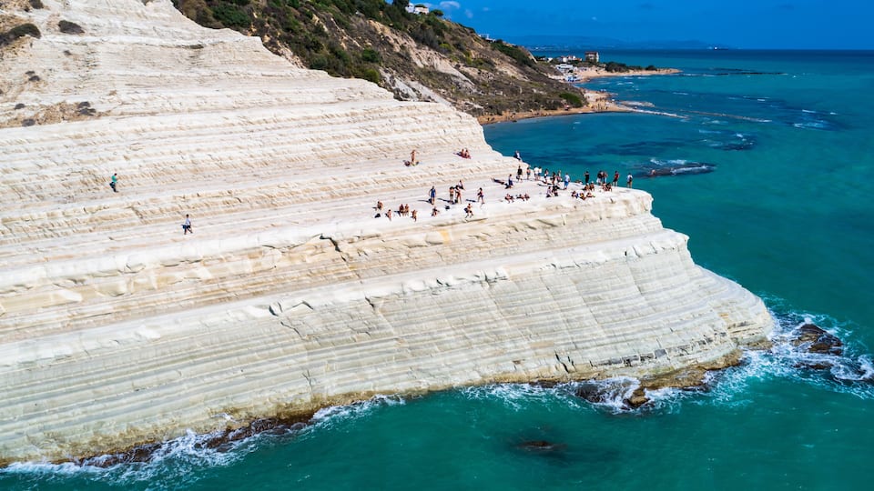 A coastal cliff with people walking and sunbathing.