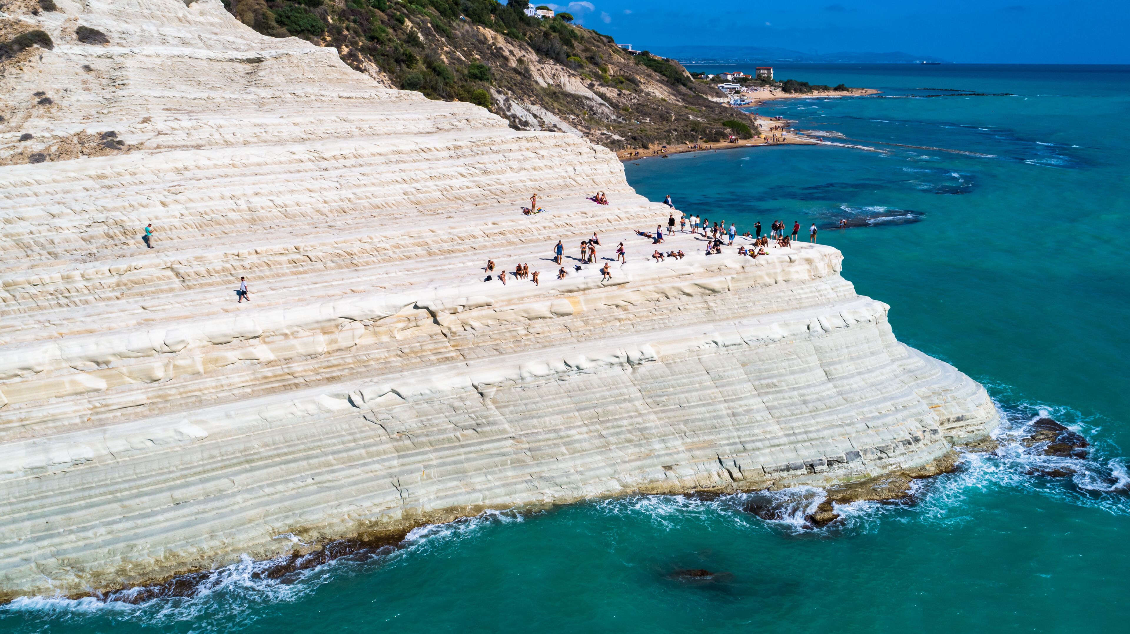 A coastal cliff with people walking and sunbathing.