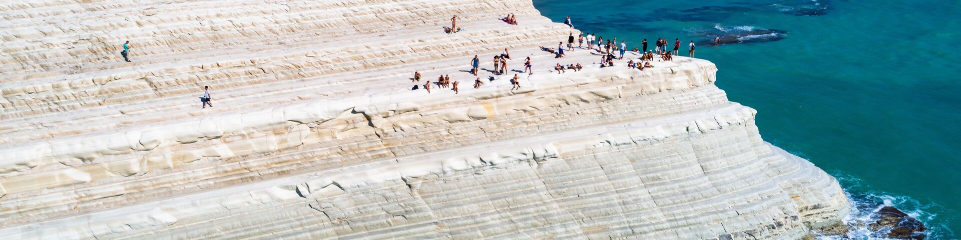 A coastal cliff with people walking and sunbathing.