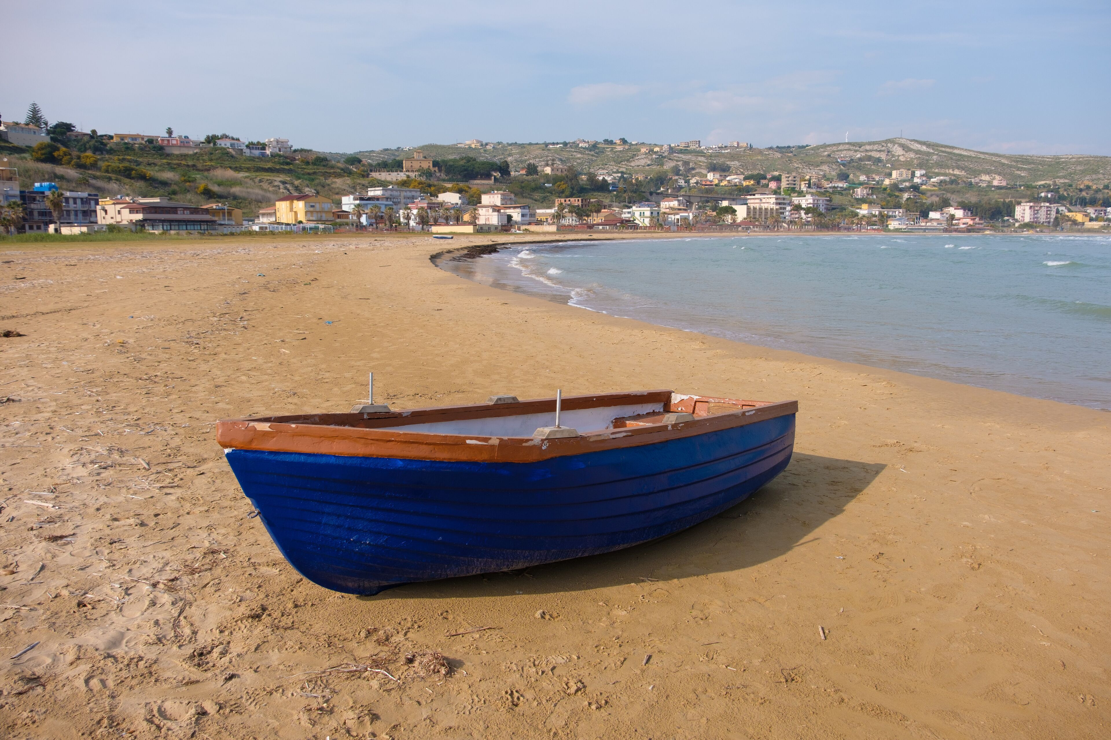 A small blue boat parked on the beach in Porto Empedocle, Sicily, under a sunny day
