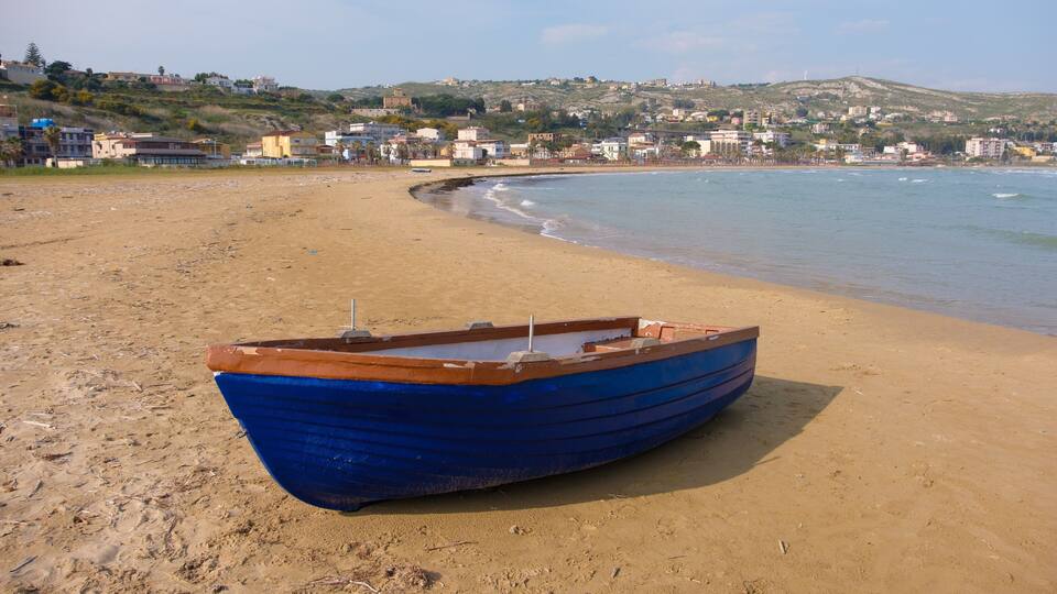 A blue boat on a sandy beach with a town in the background.