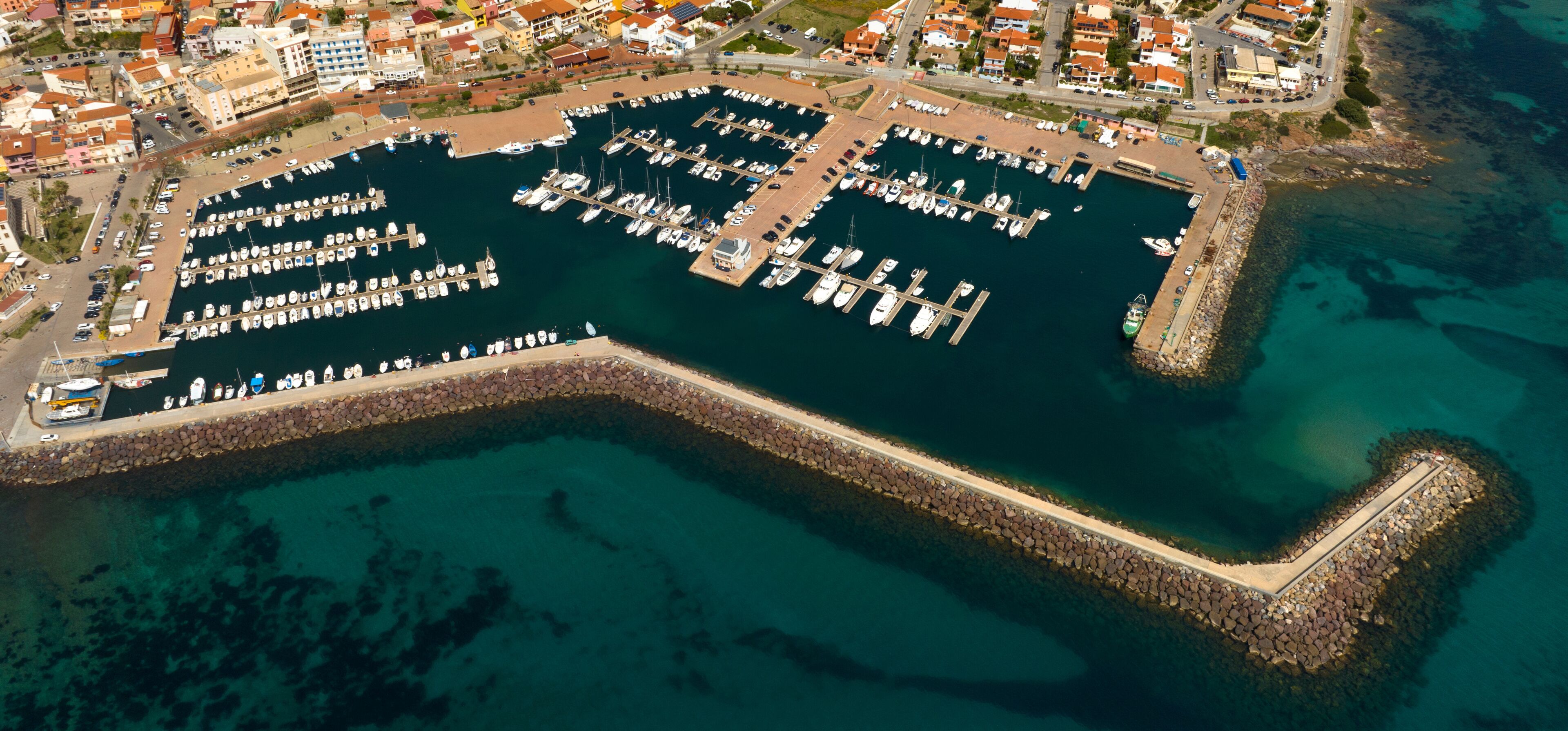 Aerial view of the marina and port of Portoscuso, in southern Sardinia, Italy. In the background the town overlooking the Mediterranean Sea. There are many boats moored at the harbour.