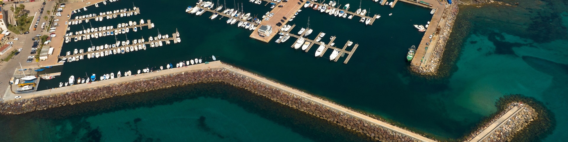 Aerial view of the marina and port of Portoscuso, in southern Sardinia, Italy. In the background the town overlooking the Mediterranean Sea. There are many boats moored at the harbour.