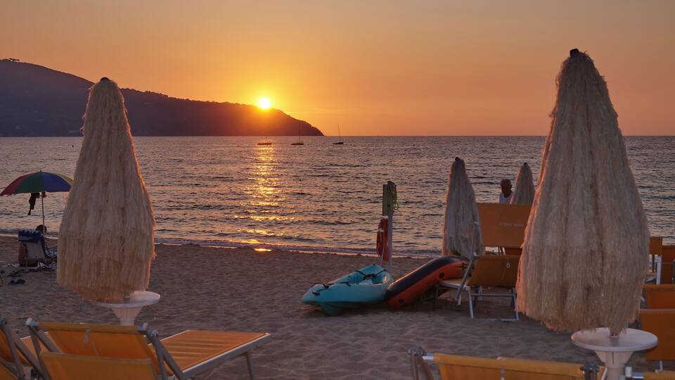 A beach at sunset with umbrellas, lounge chairs, and a lifeguard stand.