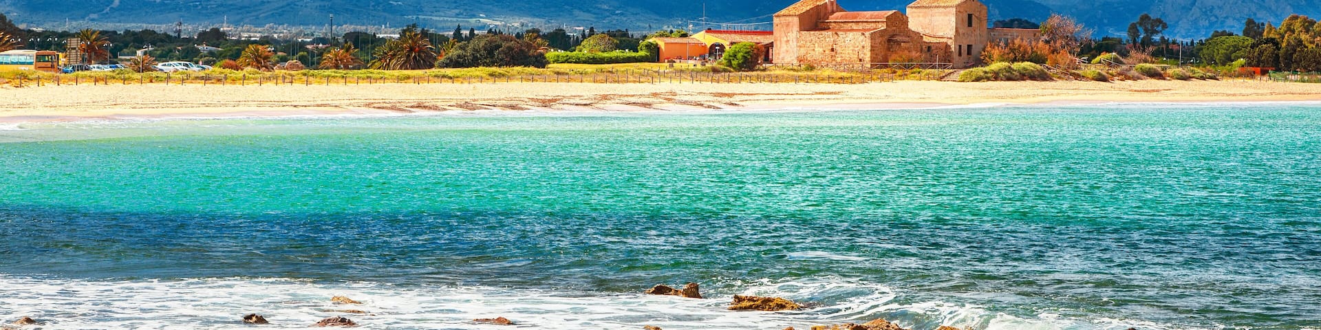 The Nora bay and beach, the medieval Sant'Efisio church near the shore and mountains in the background
