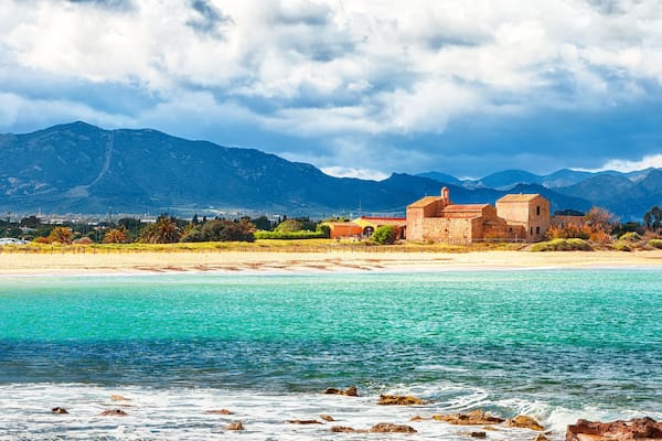 Paesaggio costiero con una spiaggia, acque turchesi cristalline e montagne sullo sfondo.