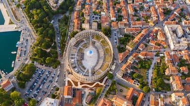 An aerial view of a city with a prominent circular structure, likely a historical site, surrounded by dense urban buildings and a waterfront.
