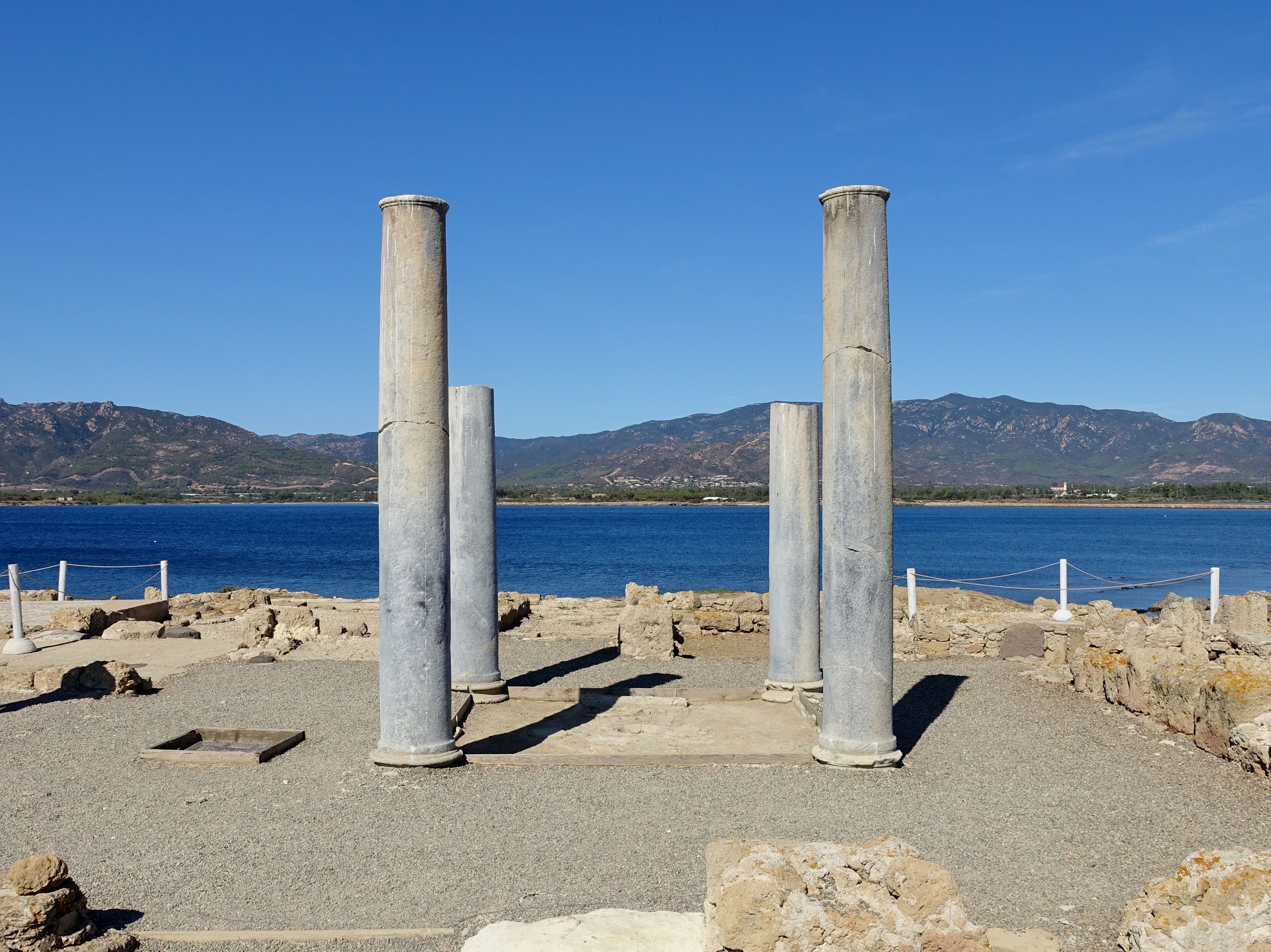 Ancient stone columns by a body of water with mountains in the background.