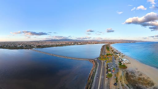 A panoramic drone shot of Viale Lungomare del Golfo, Cagliari, shows the Tyrrhenian Sea on one side and Saline di Quartu Sant'Elena on the other, under a golden hour sky with a few clouds.