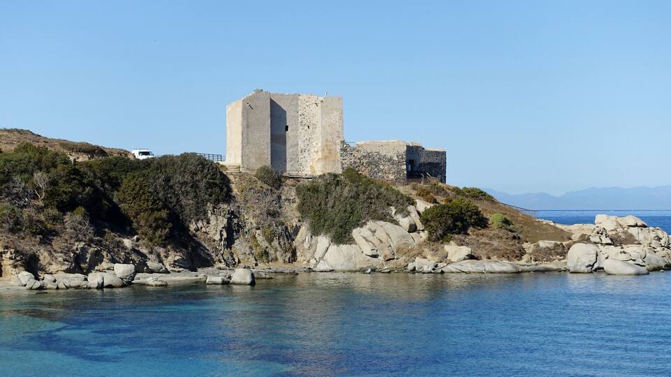 A coastal castle on a rocky cliff overlooking a clear blue sea.