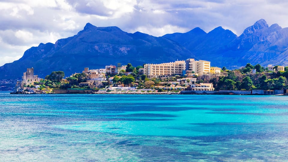 A coastal town with buildings and mountains in the background.