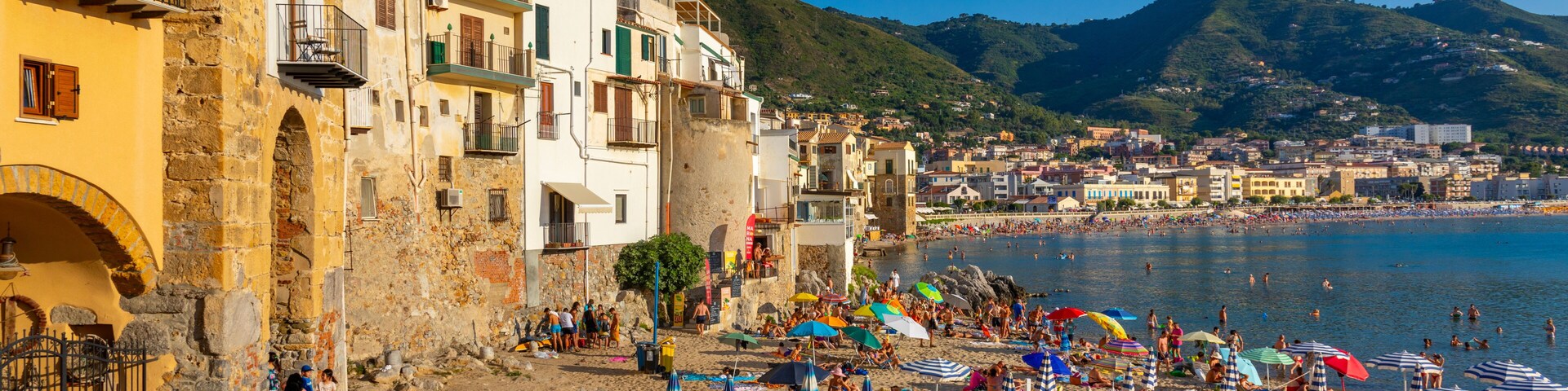 Un pueblo costero con edificios históricos, una playa de arena y un mar azul cristalino.