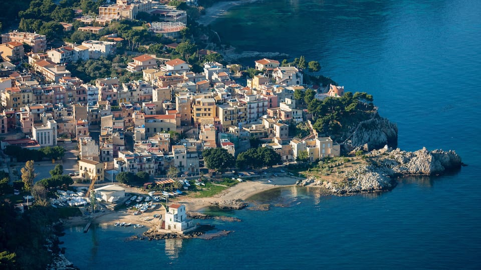 A coastal town with buildings along the shoreline and a rocky outcrop in the water.