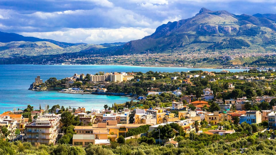A coastal town with a mountain in the background and a clear blue sea.