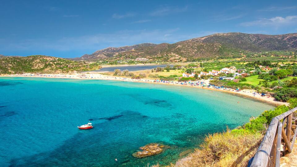 A coastal town with clear turquoise waters, a boat, and a mountainous backdrop.