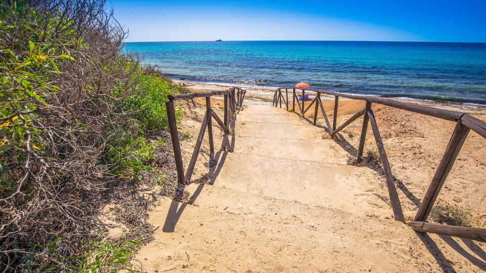 A sandy beach path leading to the ocean with a wooden railing.