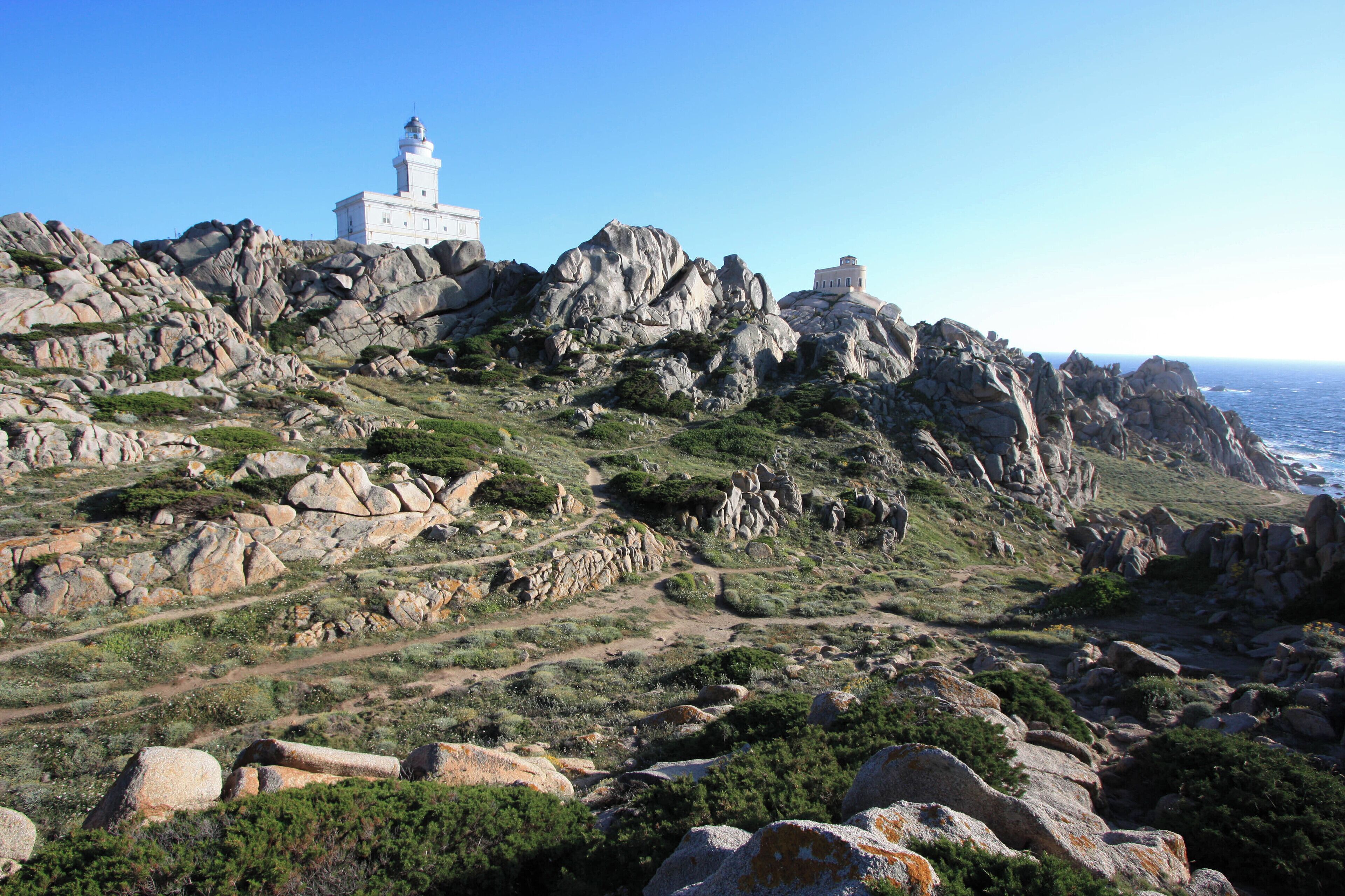A rocky coastal landscape with a lighthouse and a white building on a hill.
