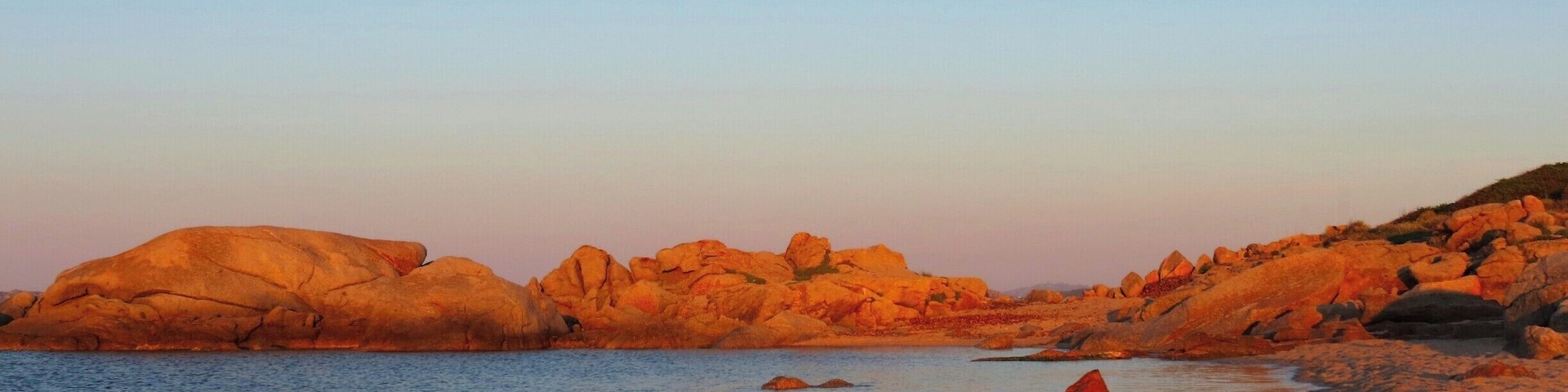 A coastal landscape with large rock formations and calm waters.