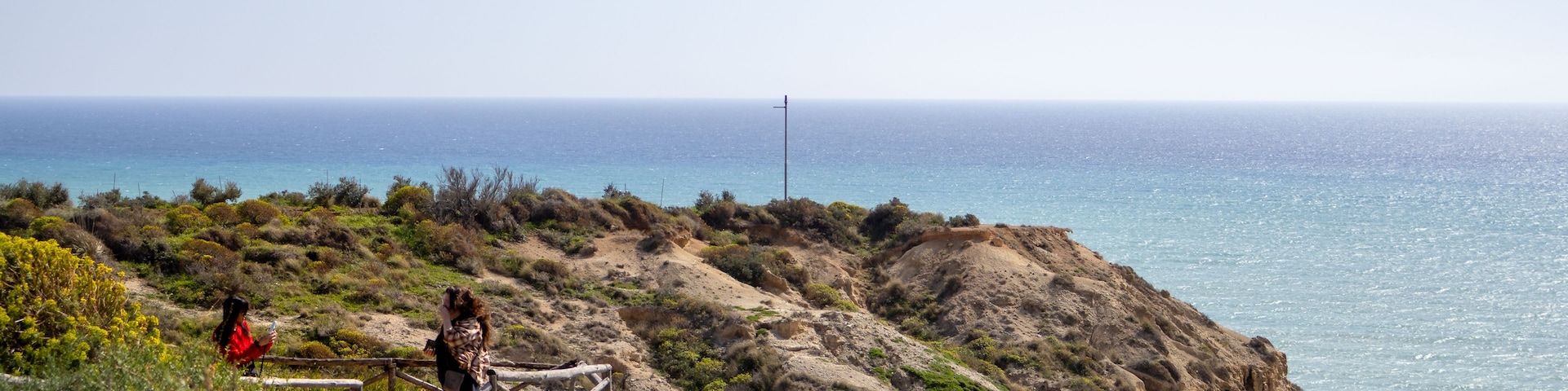 Un paisaje costero con una persona fotografiando, una cerca de madera y una vista despejada del océano.