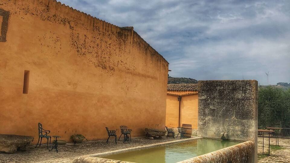 A courtyard with a fountain, outdoor seating, and a building with a weathered facade.