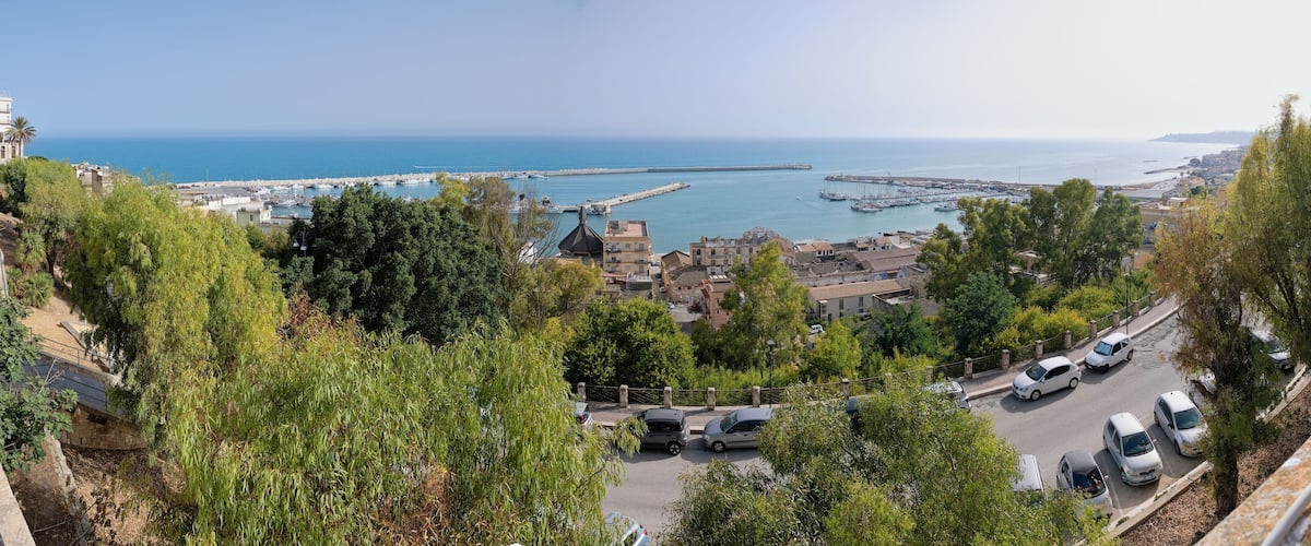 A coastal town with a marina, parked cars, and a clear view of the sea.