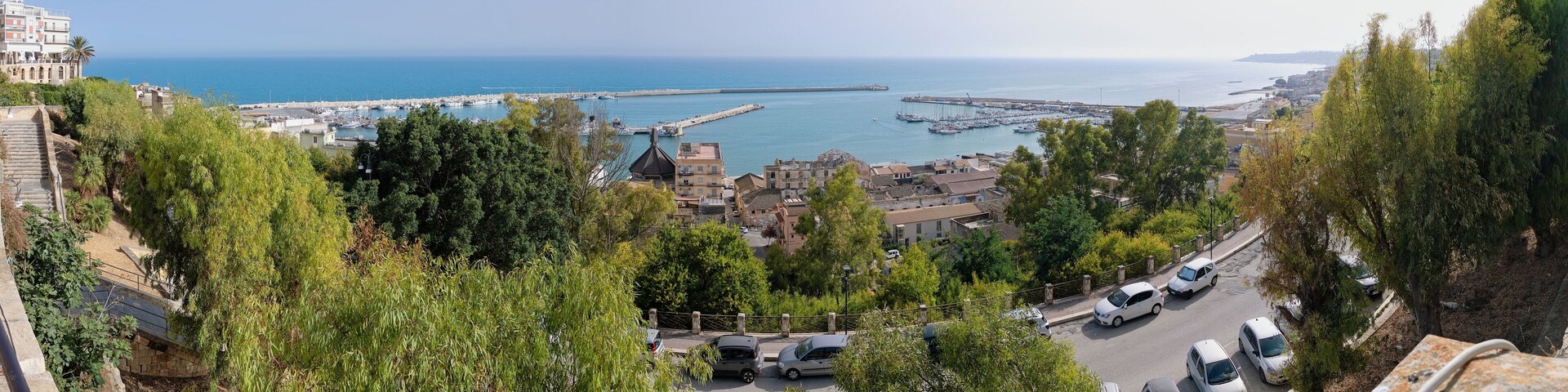 A coastal town with a marina, parked cars, and a clear view of the sea.