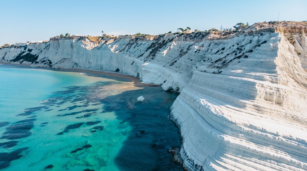 A coastal cliff with white stratified rock layers and clear turquoise waters.