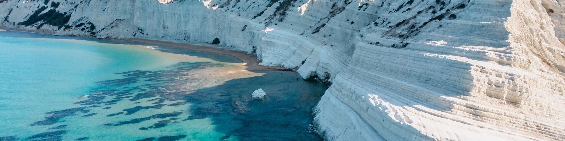 Un acantilado costero con capas blancas de roca estratificada y aguas turquesas cristalinas.