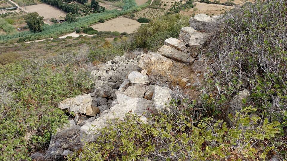 A rocky terrain with a view of a valley with fields and buildings.