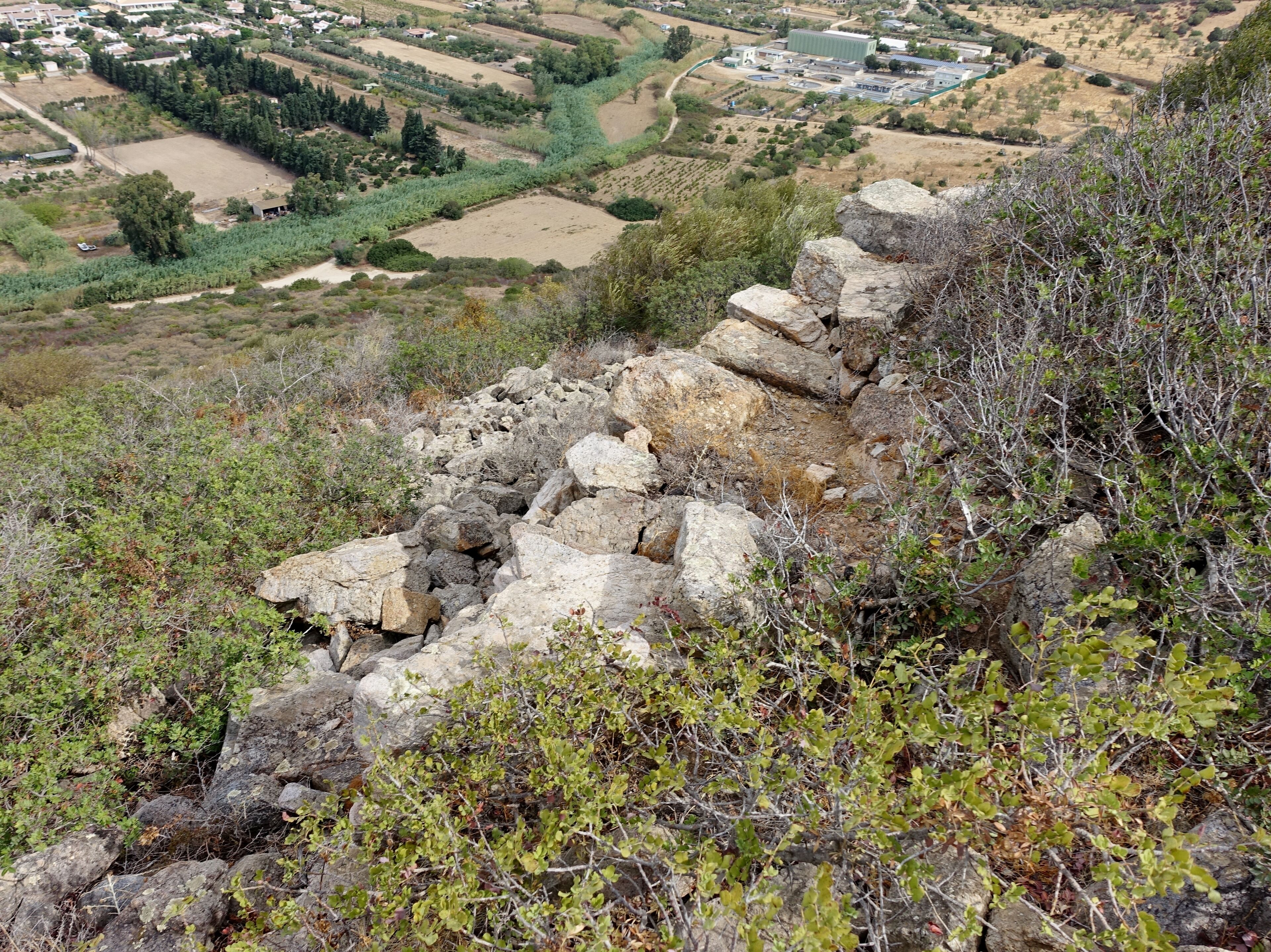 A rocky terrain with a view of a valley with fields and buildings.