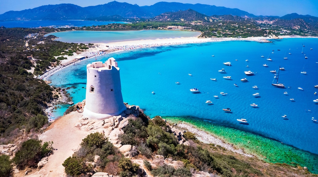 Ancient Saracen tower overlooking the turquoise waters of Porto Giunco beach in Villasimius, Sardinia. Aerial view of the historic coastal watchtower and crystal clear Mediterranean sea.