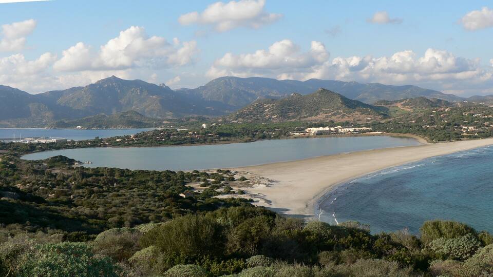 A coastal landscape with a sandy beach, a bay, and mountains in the background.