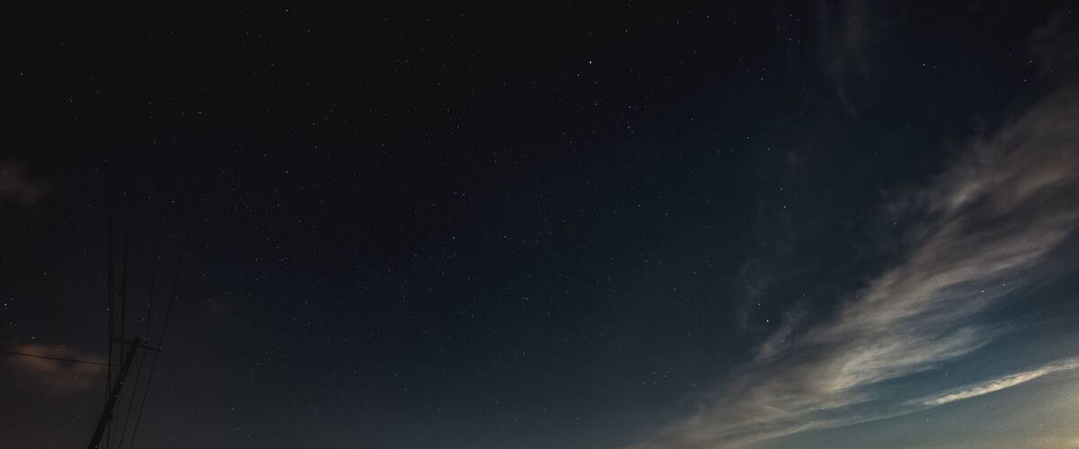 A night sky with stars, a cloudy sky, and a mountain range in the distance.