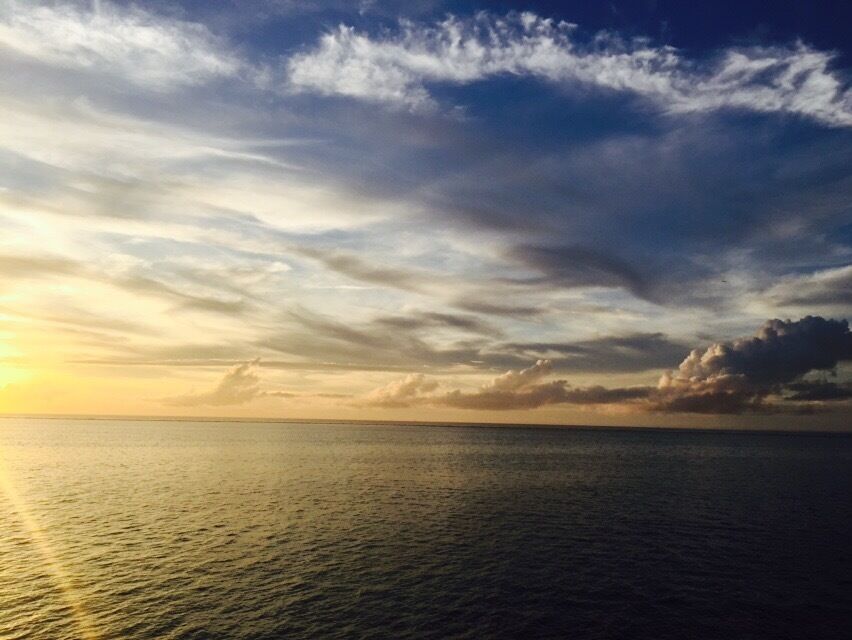 A sunset over a calm sea with a clear sky and scattered clouds.