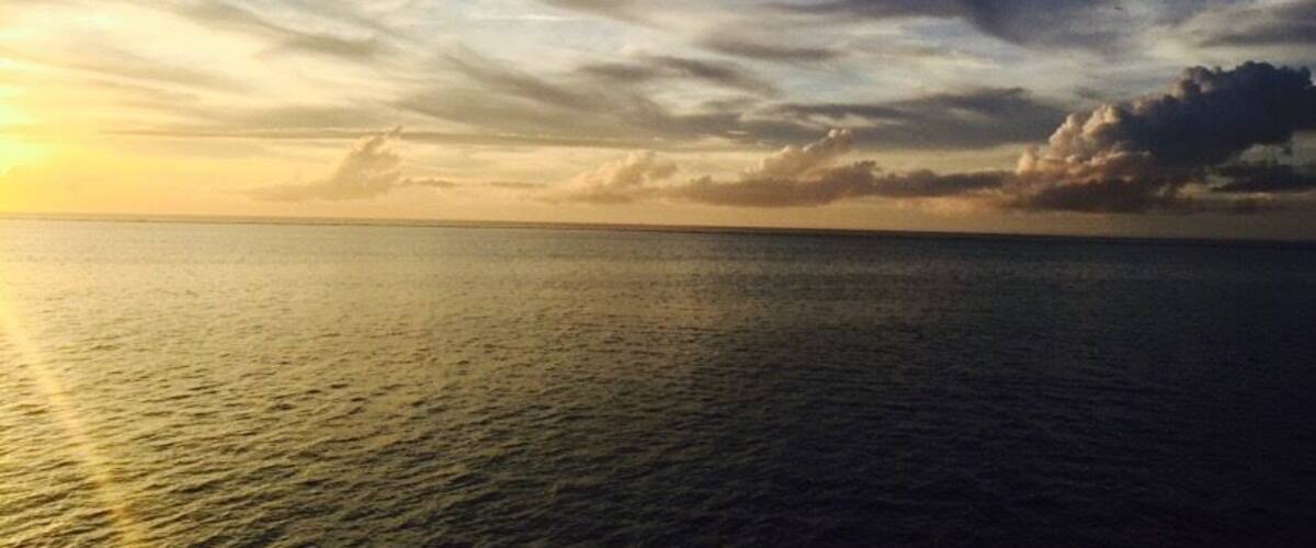 A sunset over a calm sea with a clear sky and scattered clouds.