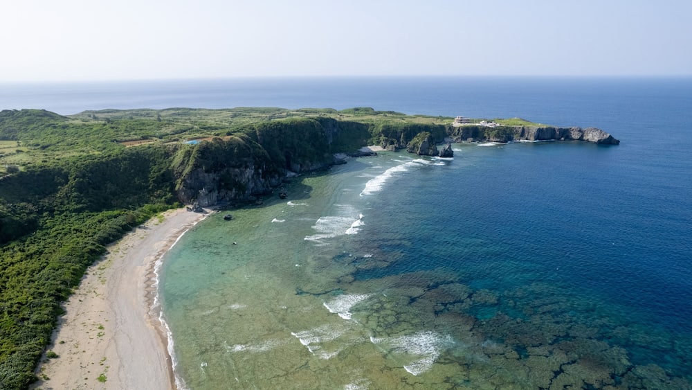 A coastal landscape with a beach, cliffs, and clear blue waters.