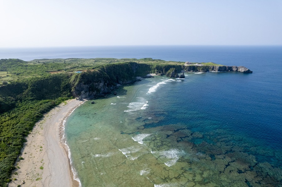 A coastal landscape with a beach, cliffs, and clear blue waters.