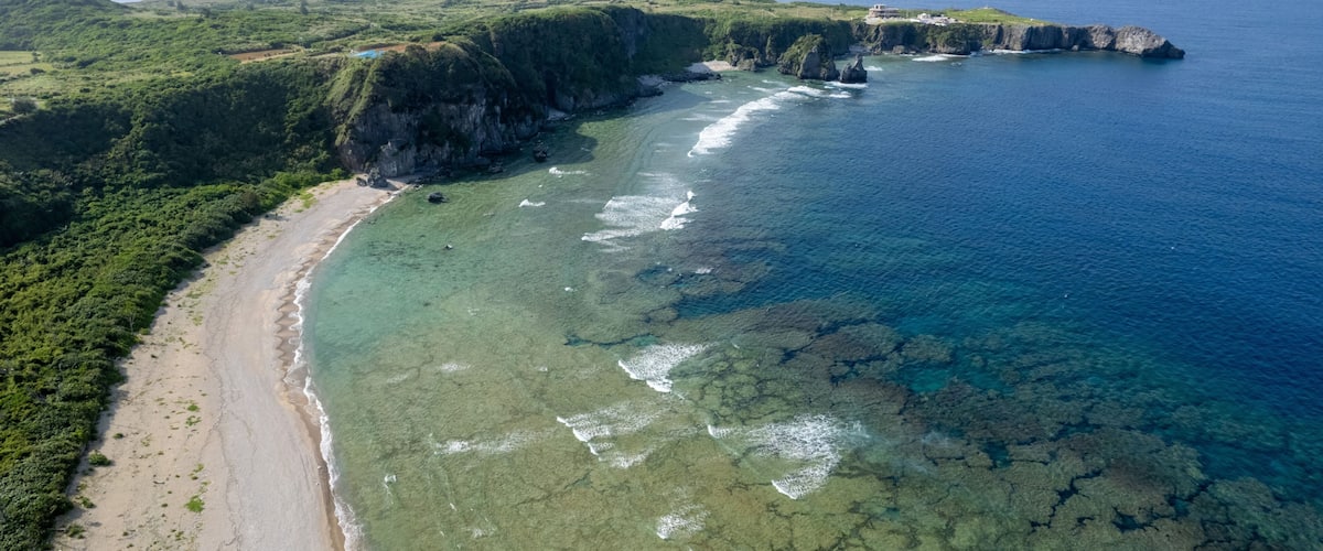 A coastal landscape with a beach, cliffs, and clear blue waters.